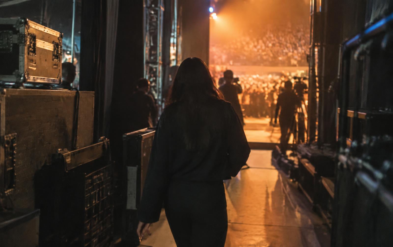 Creator walking from backstage toward a warm-lit audience